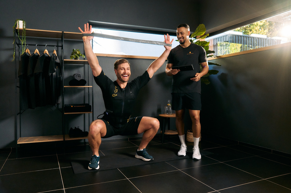 Man training with a personal trainer in a SYMBIONT EMS studio, showcasing positive energy, motivation, and personalized training and coaching.